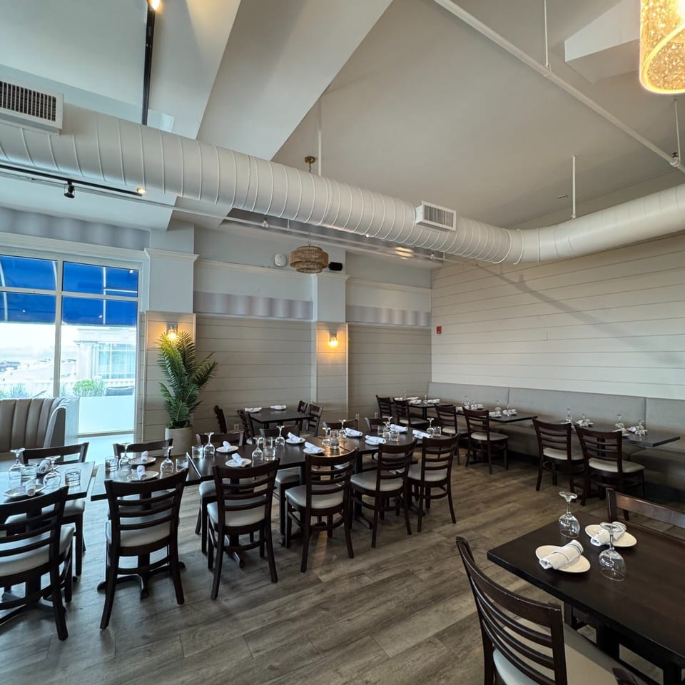 A spacious, modern restaurant dining room with dark wood tables, chairs, and light wood flooring.