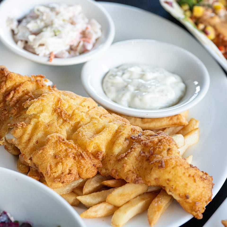 Golden-fried fish and chips with tartar sauce and coleslaw on a white plate.