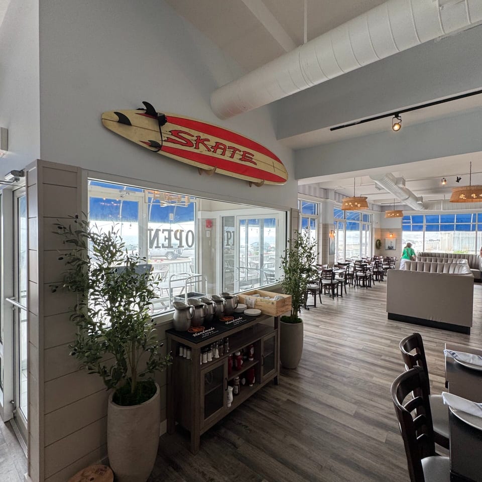 A restaurant interior with a surfboard decor, buffet station, and dining tables with ocean views.