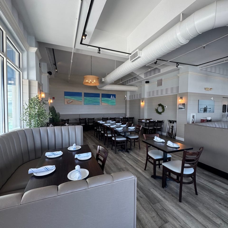 Spacious, empty restaurant dining room with booths, tables, and beach-themed artwork on the walls.